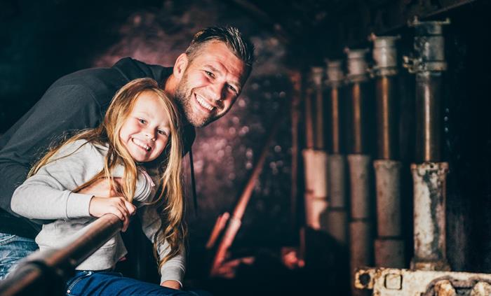 a father and young daughter look along a line of modern pit props, steel bars used to hold up the roof in a coal mine. They are in the King Coal exper